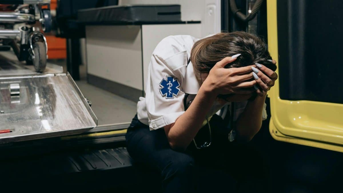 EMT in distress sitting inside an ambulance, head in hands signifying stress and exhaustion.