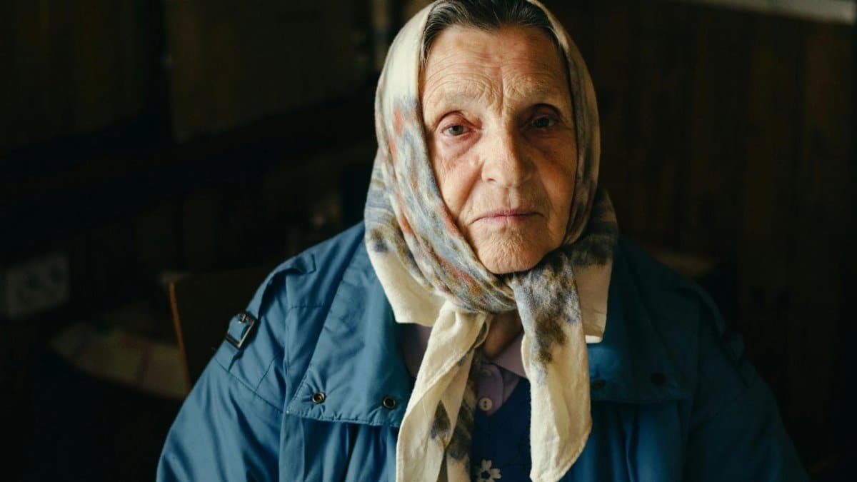 Portrait of an elderly woman wearing a headscarf indoors, showcasing wisdom and resilience.