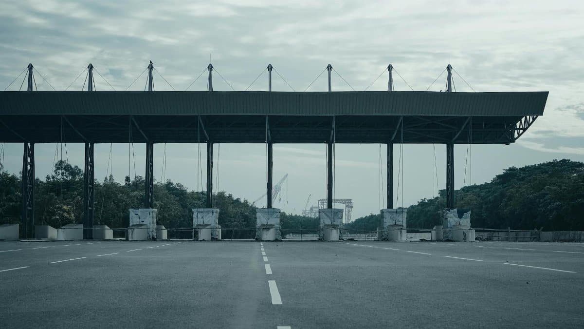 Empty toll gate on a deserted highway with overcast skies and surrounding greenery.