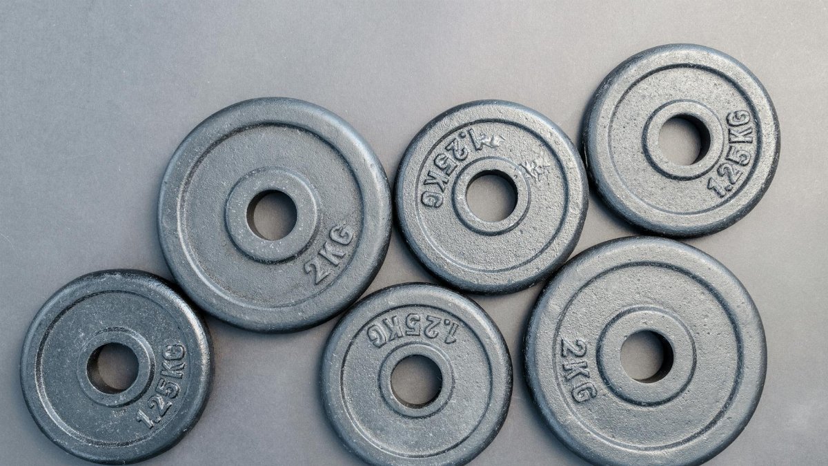 Close-up of steel gym weight plates in various sizes arranged on a gray surface.