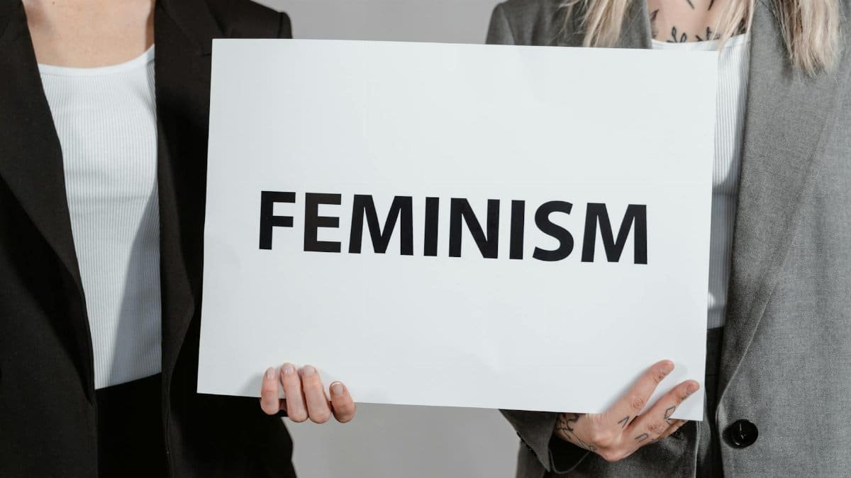 Two women in business attire holding a sign promoting feminism, emphasizing empowerment and equality.