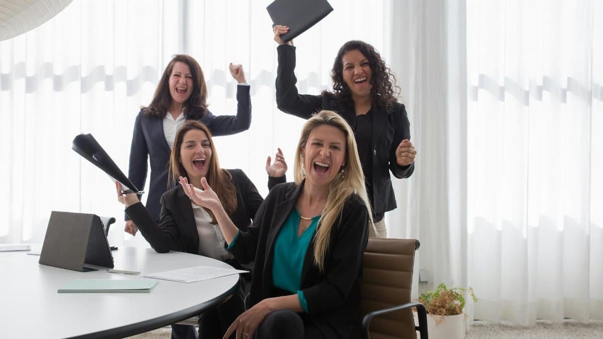 Four women in an office celebrating success and teamwork with enthusiasm.