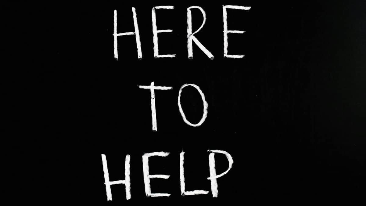 White text 'Here to Help' on a minimalist black chalkboard background, conveying encouragement and support.