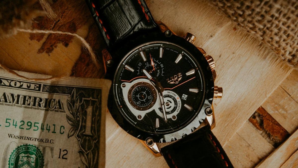 Close-up of a luxury wristwatch with a dollar bill on a wooden surface.
