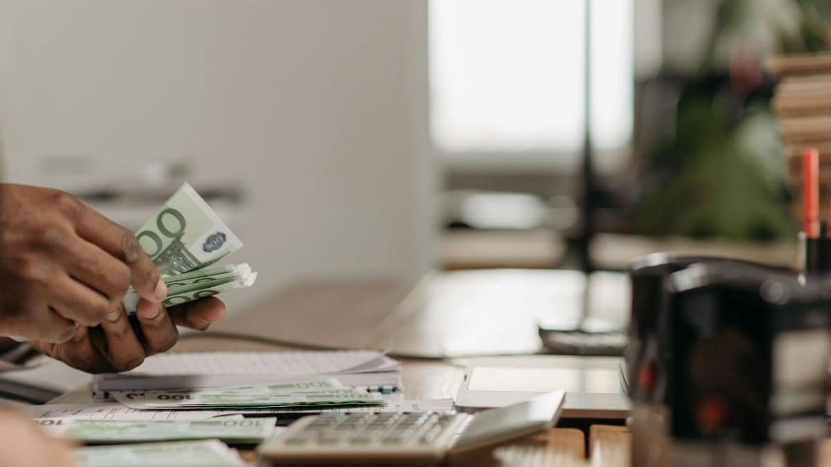 Close-up of hands counting euro bills at an office desk with a calculator.