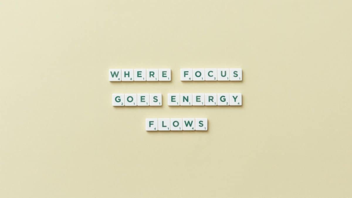 Inspirational quote 'Where Focus Goes Energy Flows' spelled with Scrabble tiles on a minimalist background.
