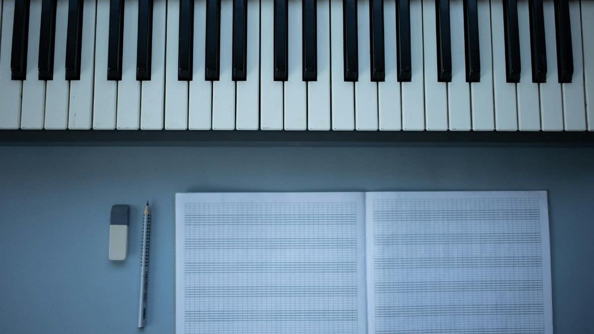 Flat lay of piano keys, sheet music, pencil, and eraser for music composition.
