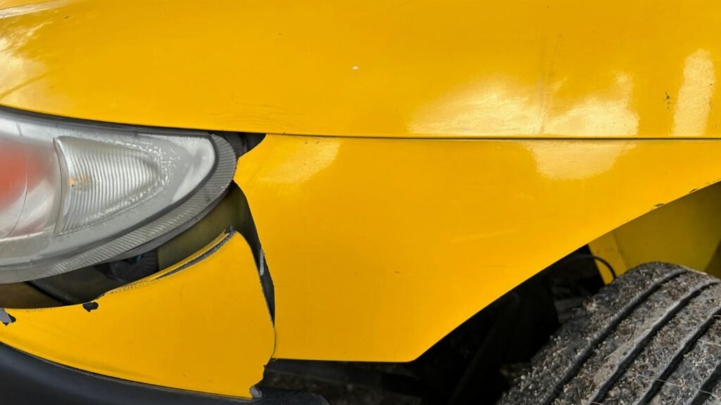 Close-up image of a yellow car's damaged front bumper and headlight for insurance or accident concept.