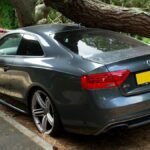 A broken Audi car crushed by a fallen tree in a UK street accident.