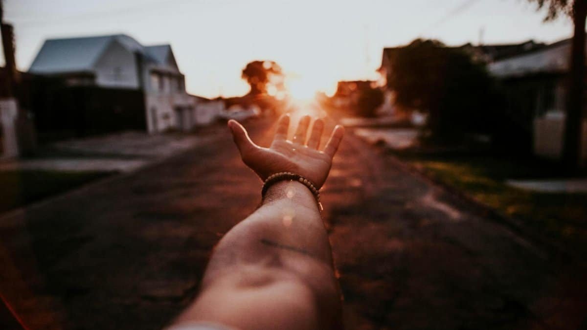Dramatic view of a hand reaching towards a sunset on a quiet urban street.