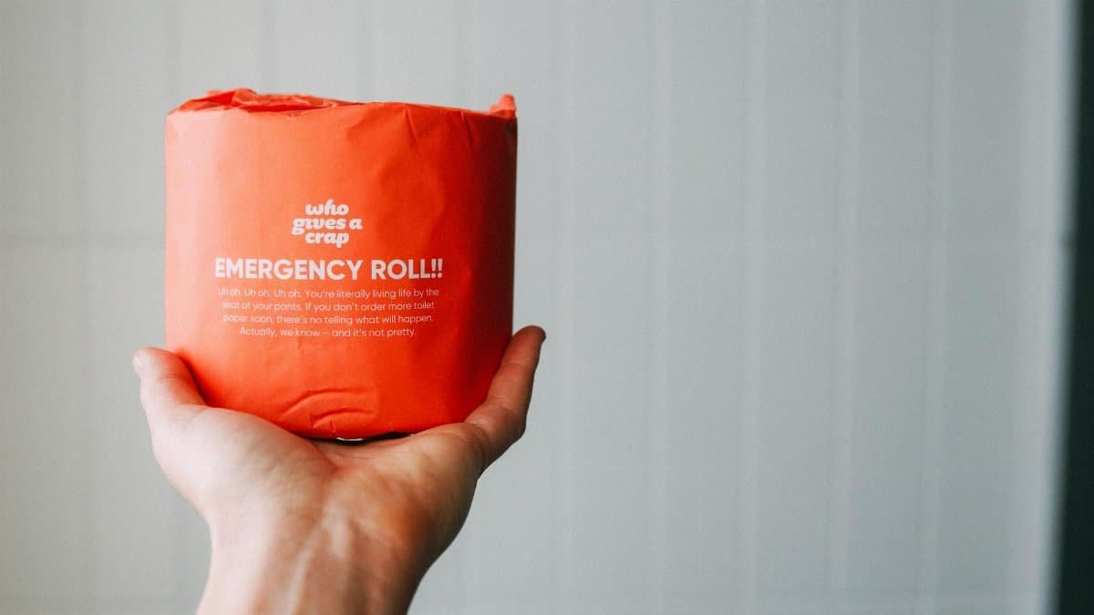 A hand holds an emergency toilet paper roll with humorous packaging, emphasizing hygiene and pandemic awareness.
