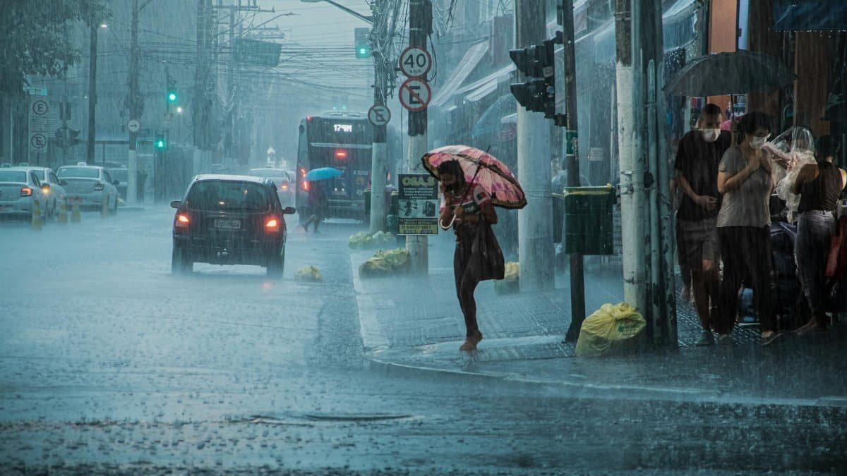 A busy urban street during heavy rain, with cars, pedestrians, and umbrellas.