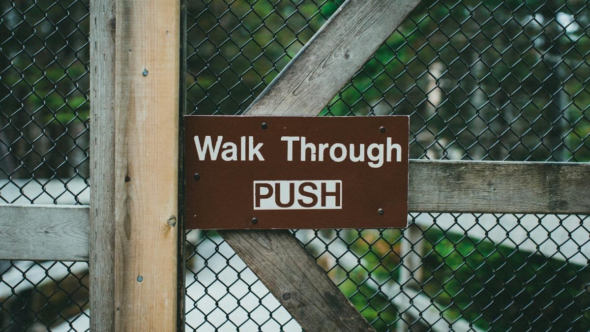 Close-up of a wooden gate with metal fence and 'Walk Through PUSH' sign.
