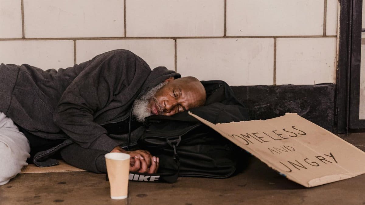 African American man sleeping in subway with sign, highlighting social issues.