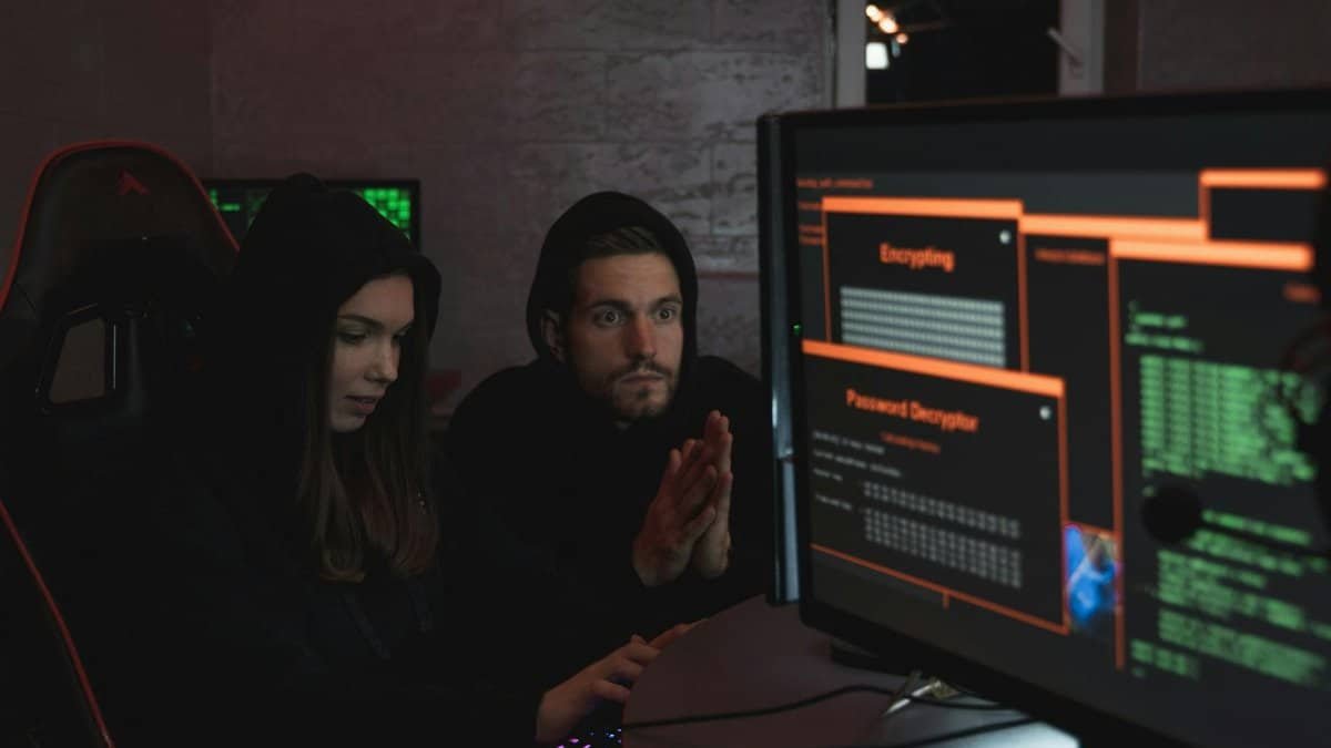 Cybersecurity experts in hoodies analyzing encrypted data on computer screens in an indoor setting.