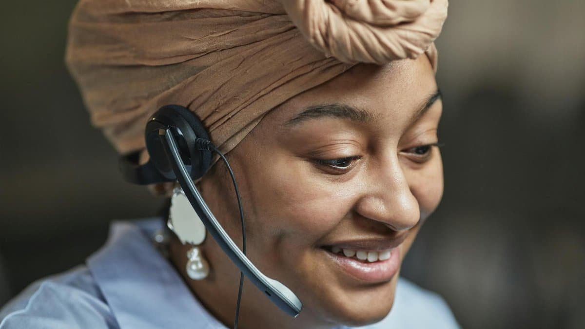 Close-up of a smiling woman in a headscarf with a headset, working in a call center.
