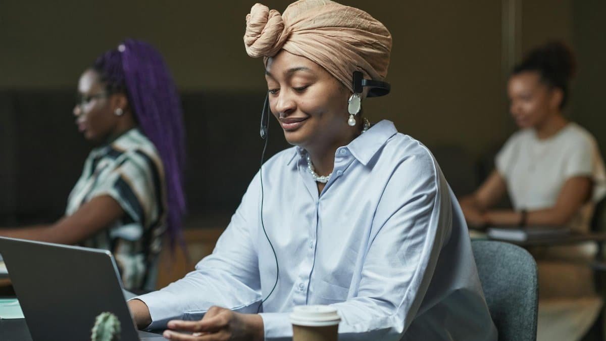 Smiling woman in headscarf working in call center on laptop with headset.