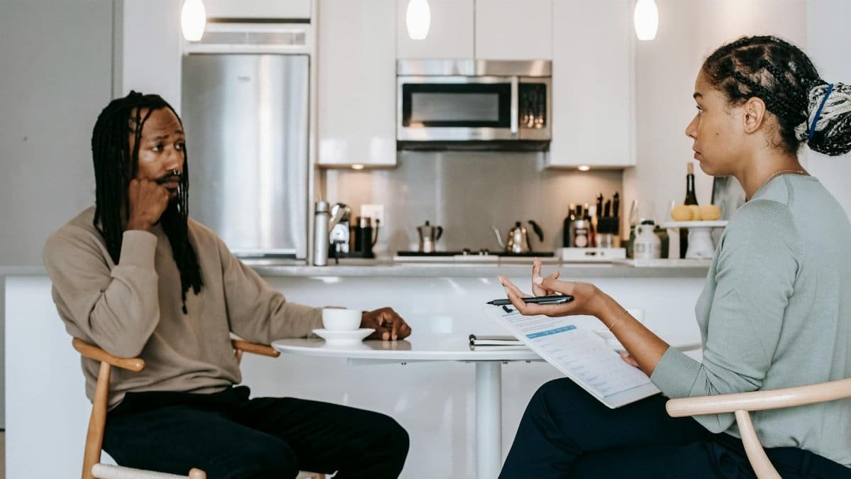 A therapist and client discussing in a contemporary kitchen, symbolizing mental health focus.
