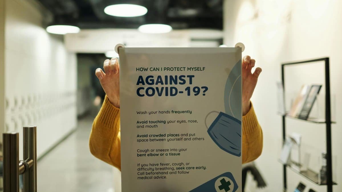 Healthcare poster with COVID-19 prevention tips held indoors, focusing on safety measures.