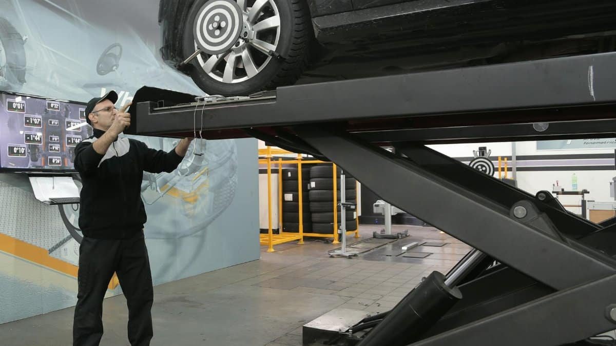 Mechanic carefully examining car on hydraulic lift in automotive workshop, ensuring safety and performance.