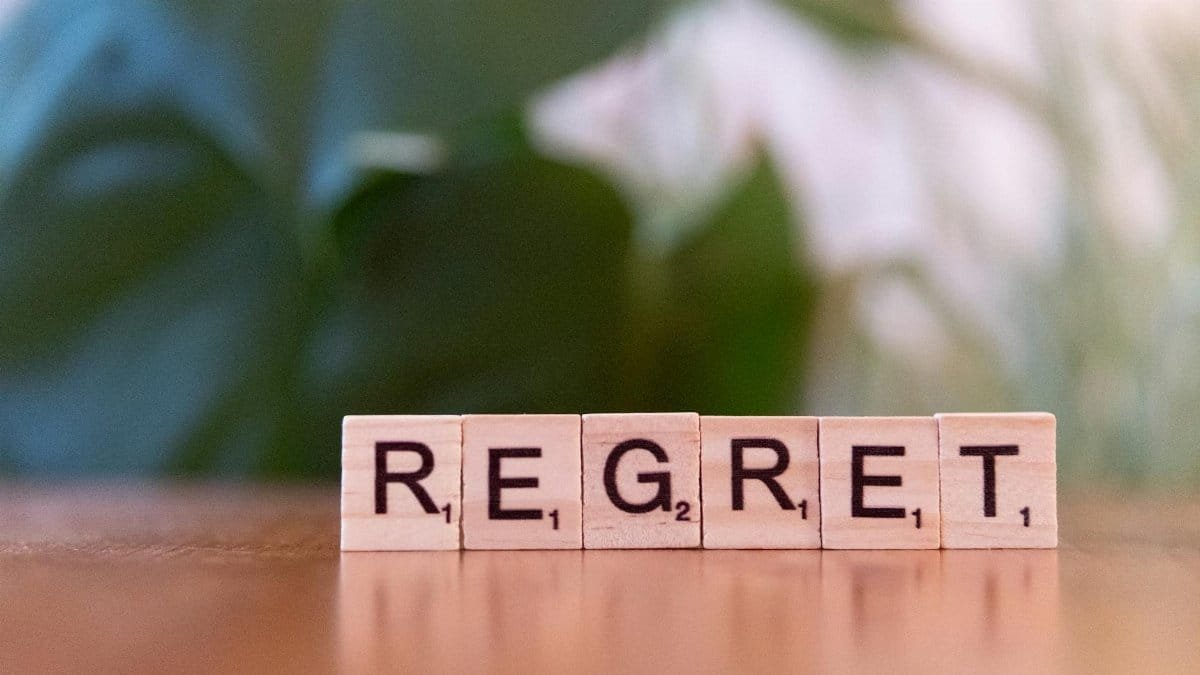 Wooden letter tiles forming the word 'Regret' on a blurred background, symbolizing emotions.