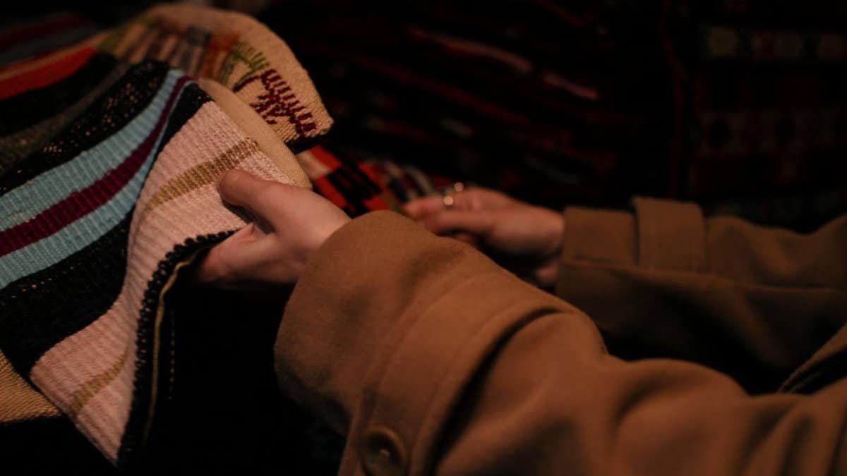 A woman examines colorful textiles in a dimly lit store, highlighting fabric selection.