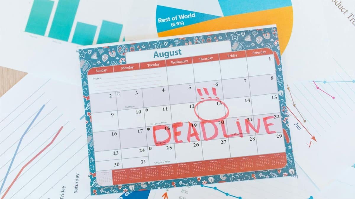 Vibrant August calendar on a desk with deadline marked in red, surrounded by graphs and charts.