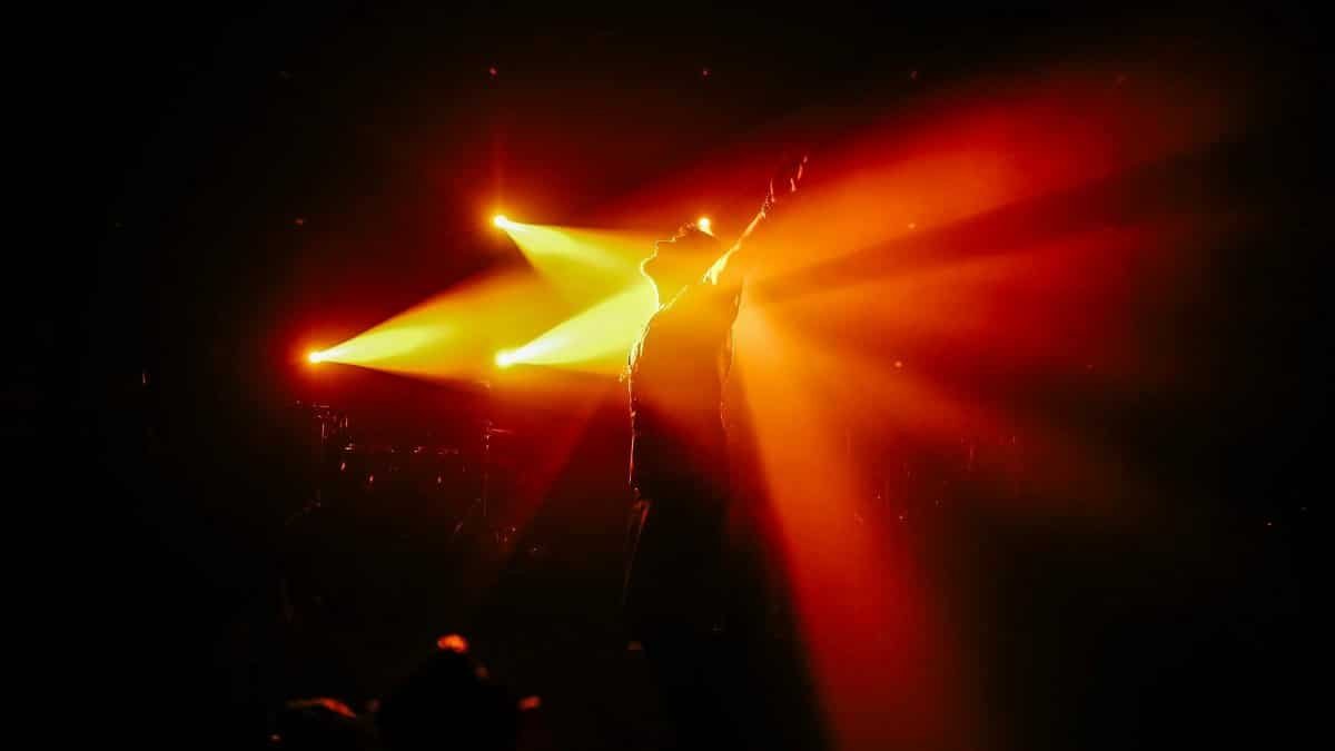 Silhouette of a performer on stage with vibrant spotlight beams creating dramatic concert atmosphere.