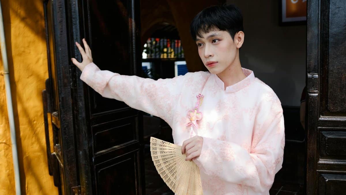 Young man in traditional pink ao dai holding a fan during a Vietnamese celebration in Bến Tre.