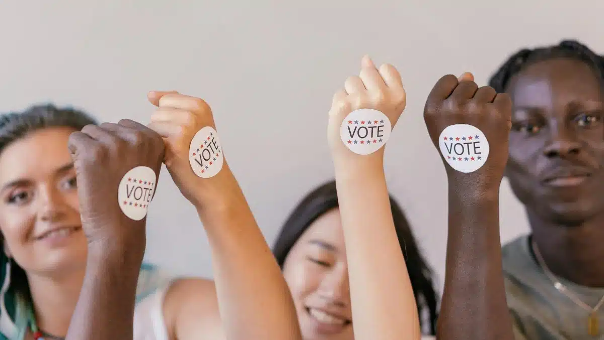 Multiracial hands with voting stickers raised in solidarity, promoting democracy.