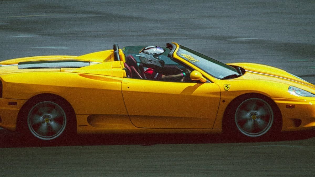 Yellow sports car in high-speed motion on racetrack with helmeted driver.