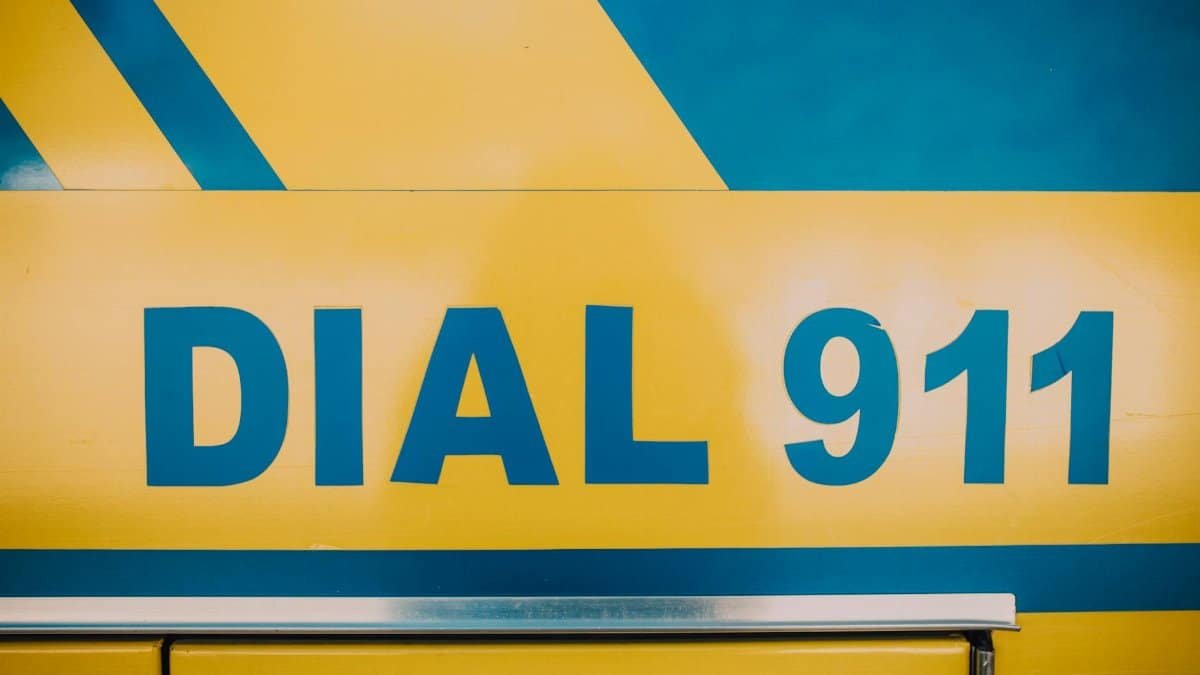 Close-up of 'Dial 911' emergency sign on a vehicle with bold yellow and blue colors.