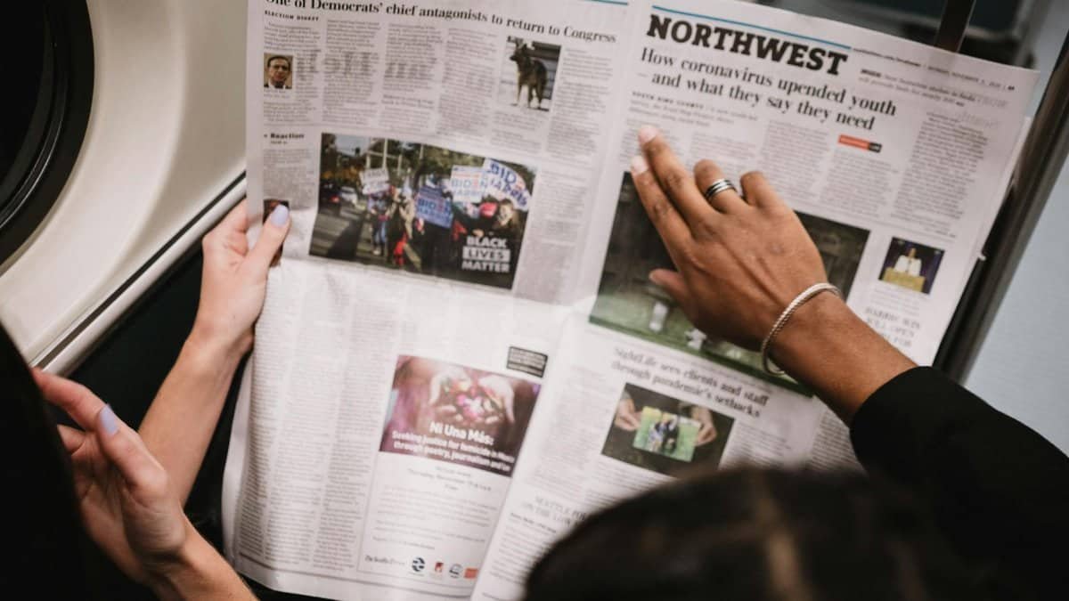 People reading a newspaper on a subway train, highlighting current events and diverse perspectives.