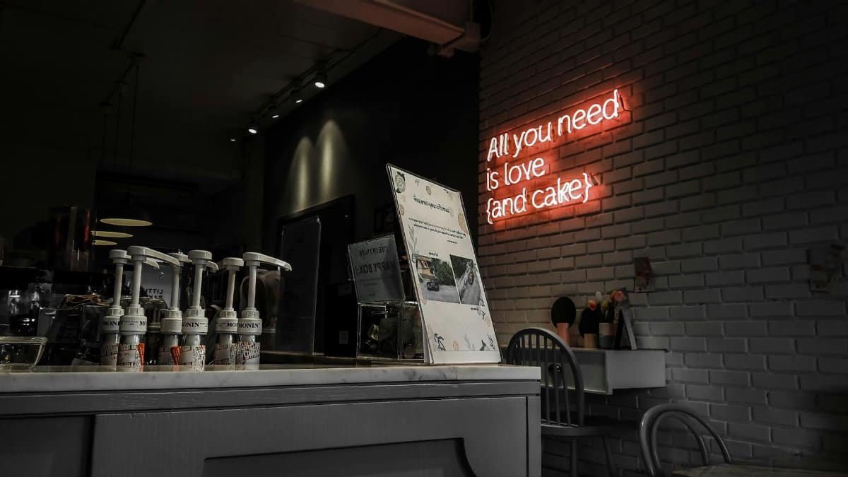 Intimate cafe setting with a neon sign reading 'All you need is love (and cake)'