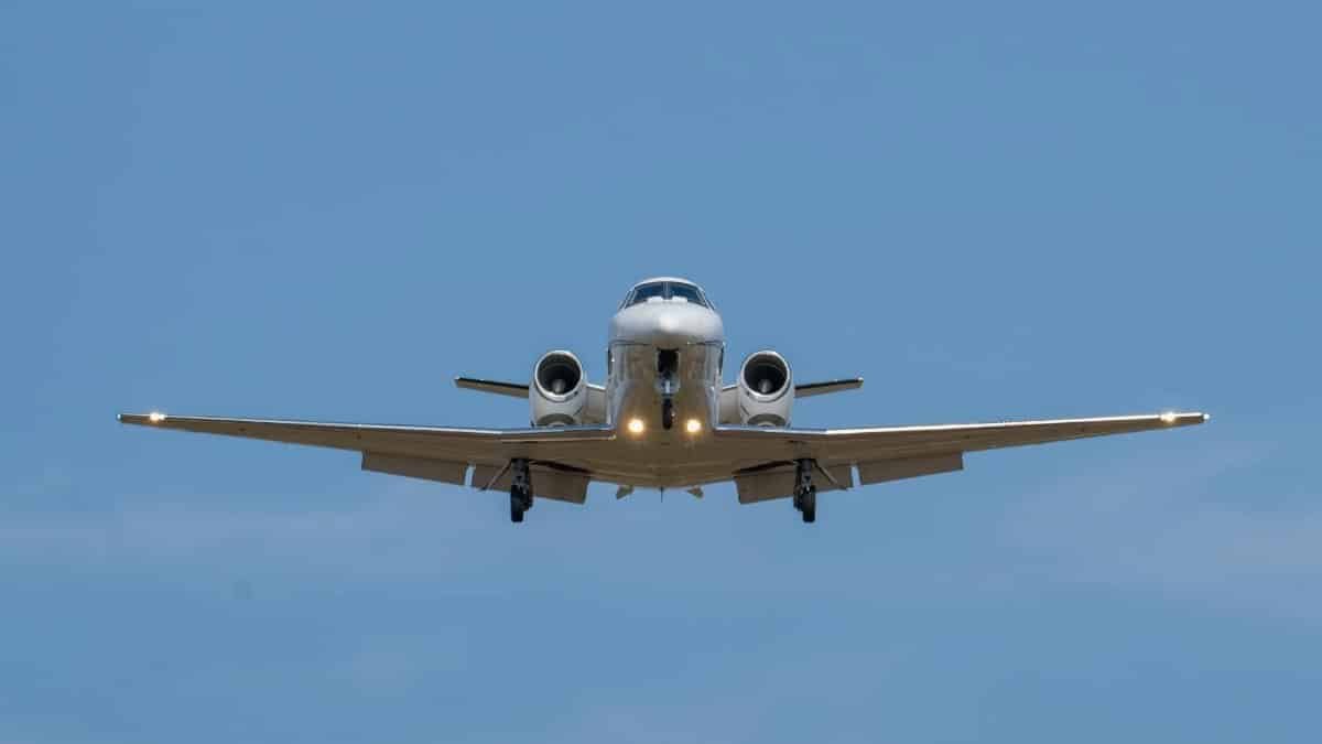 A private jet in flight against a clear blue sky, captured on final approach.