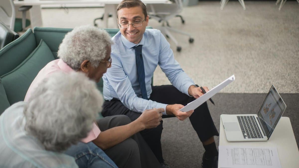 Consultant discussing financial plans with senior clients in a modern office setting, using documents and a laptop.