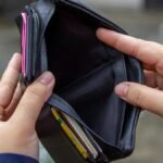 An outdoor image of hands holding an empty black wallet, suggesting financial scarcity.