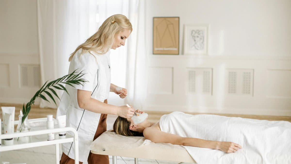 Aesthetician providing facial care treatment to a woman in a serene spa environment.