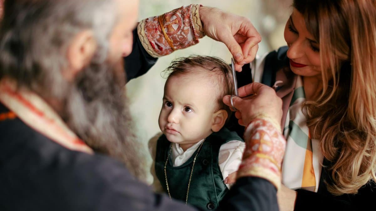 A baby's first haircut performed during a religious ritual with parents and clergy present.