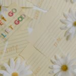 Flat lay of daisies and motivational notes with phrases like 'Let Go Let God' on a white background.