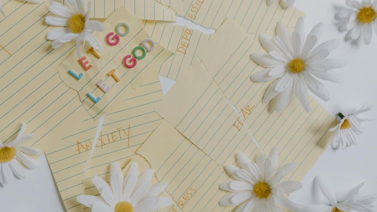 Flat lay of daisies and motivational notes with phrases like 'Let Go Let God' on a white background.