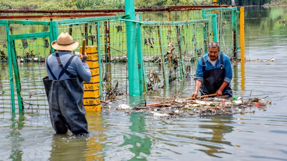 Two men working to clear trash from a flooded area, focusing on water pollution and urban flooding.