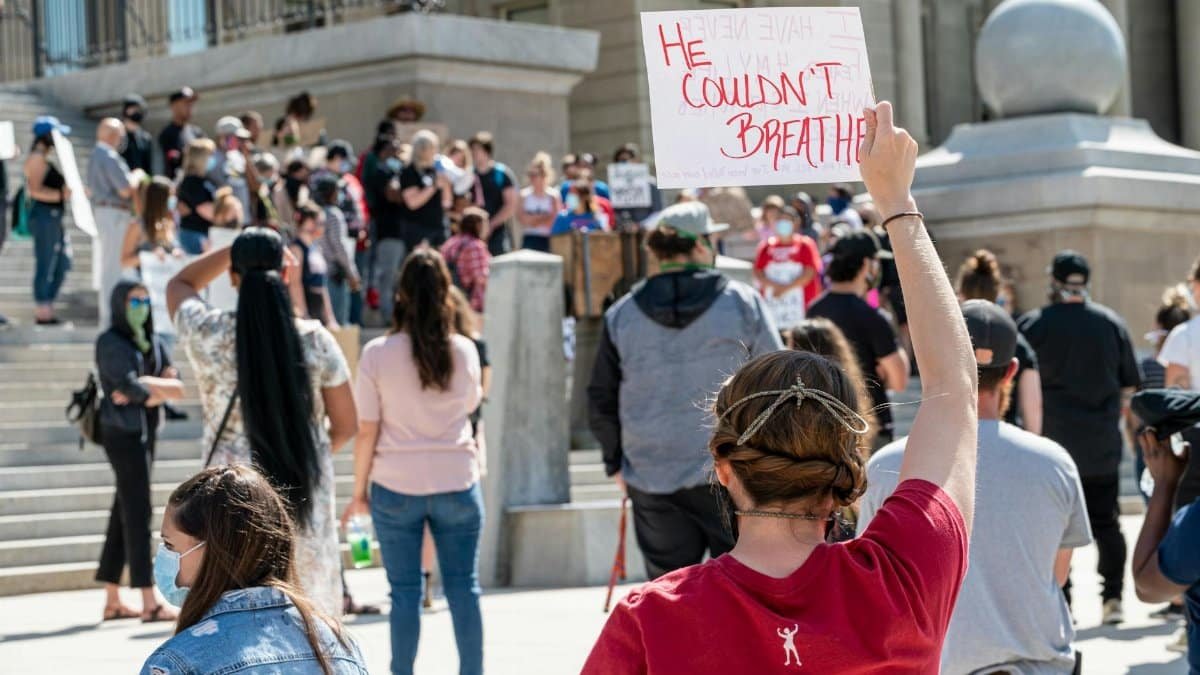 Multiracial crowd of activists with placard saying He Couldnt Breathe gathering outside government building on sunny day