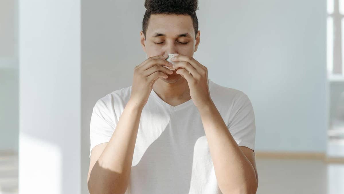 A man sneezing into a tissue, illustrating symptoms of flu or allergies.