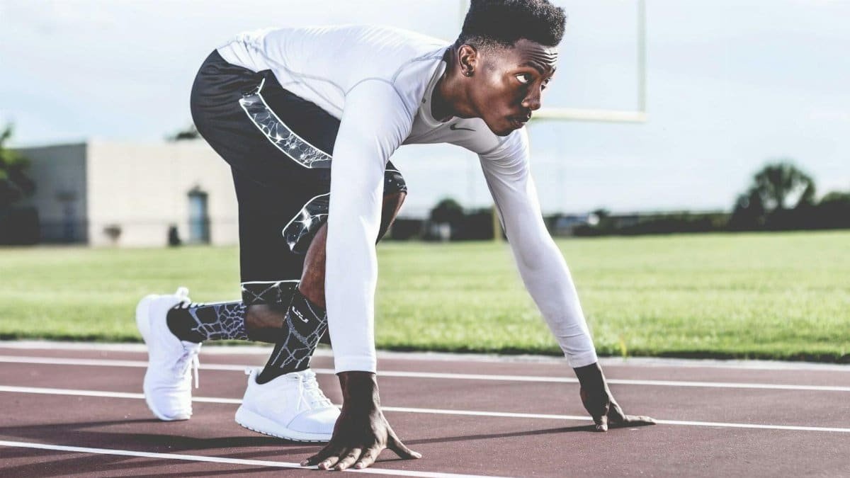 Focused athlete in starting position on a sunny track field, ready to sprint.