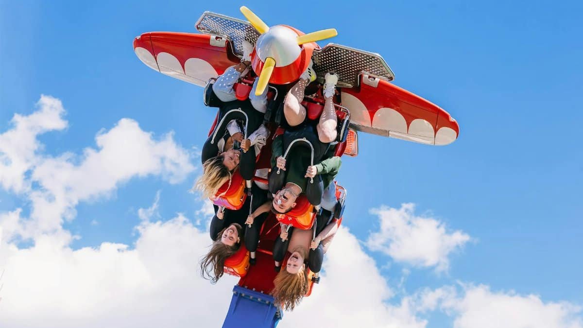 Group of friends enjoying an upside-down amusement park ride against a bright blue sky.