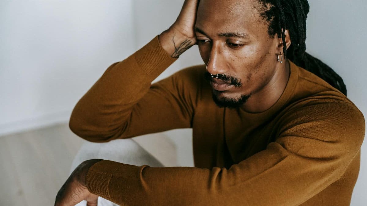 A contemplative man with dreadlocks sits indoors, expressing introspection and solitude.