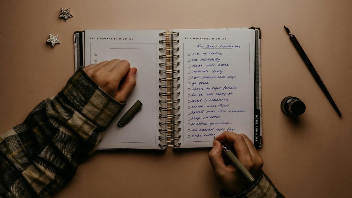 Overhead shot of a person writing New Year's resolutions in a notebook on a desk.