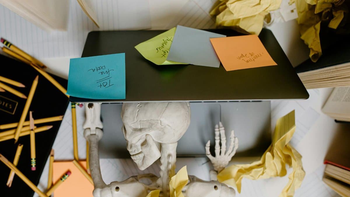 A striking visual of a skeleton at a laptop surrounded by notes and paper, symbolizing work burnout.