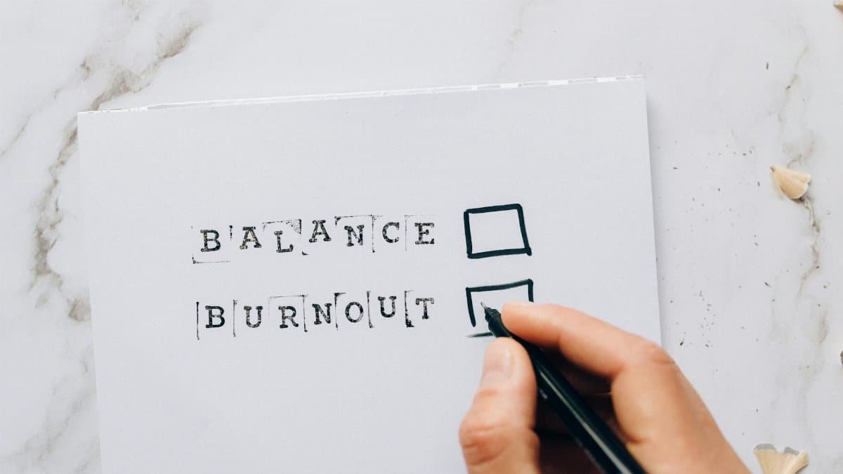 Close-up of a hand hovering over a checklist with options for balance or burnout, symbolizing stress and choice.